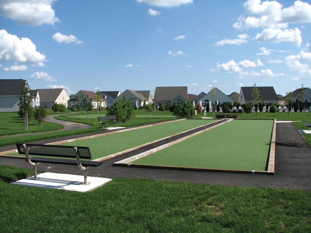 Community bocce ball courts featuring professional artificial turf installation, with neatly bordered playing surfaces, surrounding walkways, and landscaped residential neighborhood setting