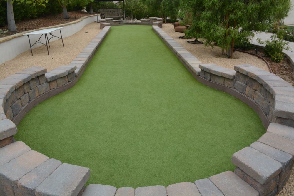 Custom artificial turf installation for a backyard bocce ball court, featuring smooth playing surface, stone retaining walls, and low-maintenance landscape design for residential outdoor recreation
