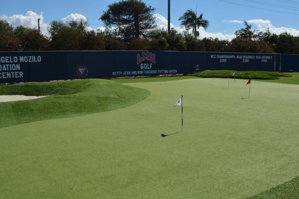 Collegiate synthetic turf putting green with contoured mounds and multiple flagsticks, designed for competitive golf training and year-round performance at a practice facility.