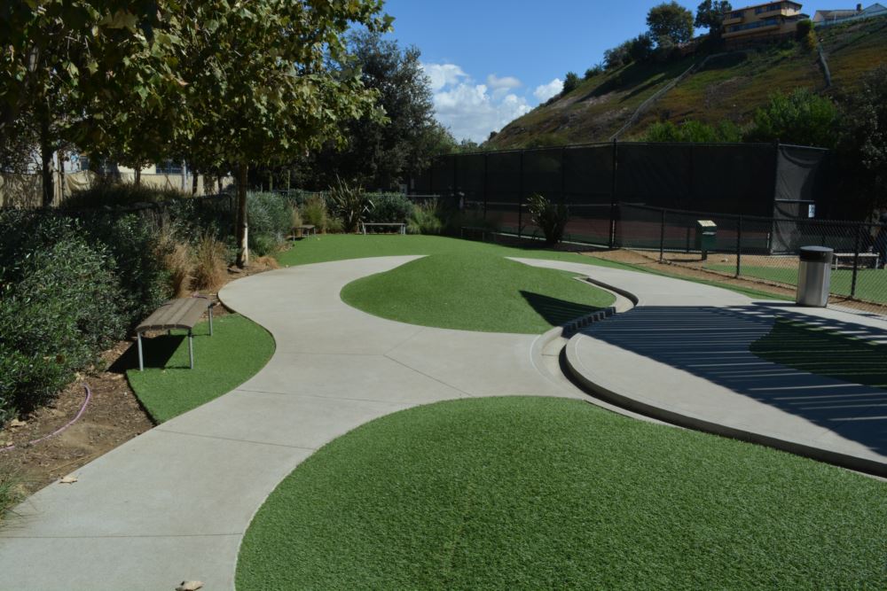 Pet-friendly park space featuring artificial turf for dogs, designed with curved concrete pathways, shaded seating, and durable, low-maintenance synthetic grass ideal for active play.