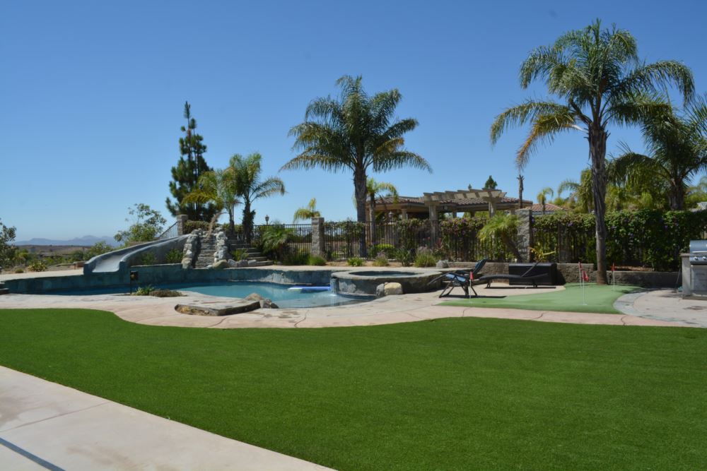 Luxury backyard featuring the best artificial turf around a custom pool and spa, with lush green synthetic grass and a private putting area for year-round outdoor enjoyment.
