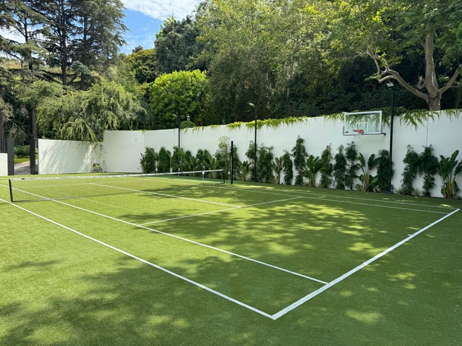 Backyard tennis court featuring premium artificial grass with integrated net and basketball hoop, surrounded by lush landscaping and privacy walls.