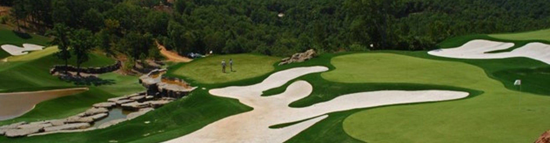 Southwest Greens artificial putting green aerial view with sweeping sand bunkers, water hazard, rock formations, and two golfers on a championship course.