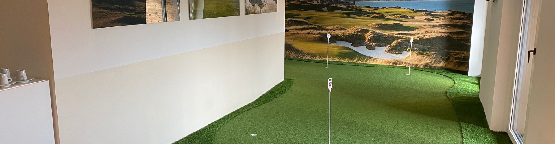 Southwest Greens indoor putting green installed in a modern office space with three holes, golf course mural wall, and framed course photography.